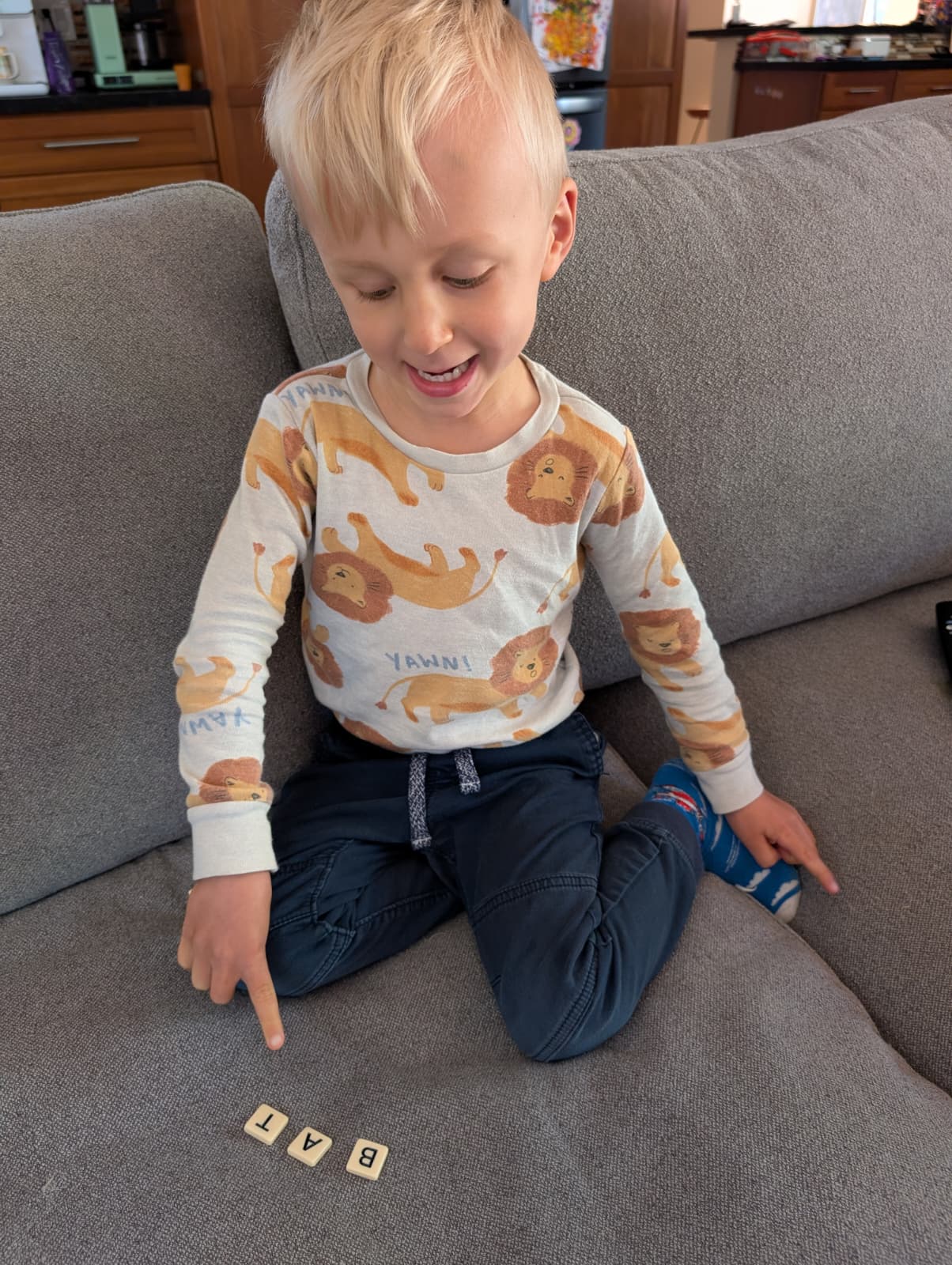 Child smiling while building a word with letter tiles on the couch